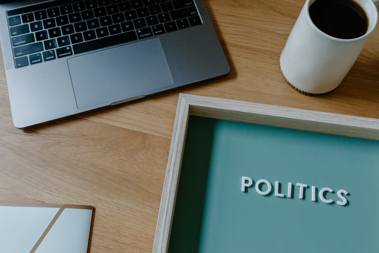 A contemporary workspace featuring a laptop, coffee cup, and a sign with the word 'Politics'.