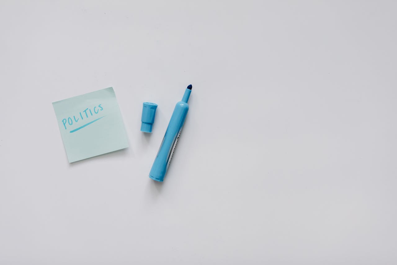 Offerings A flat lay of a blue marker and sticky note with 'politics' on a white surface.